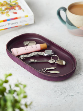 "Beautifully hand-dyed leather catchall trays in a deep purple pill shape, ideal for keeping small items like keys, cufflinks, or sunglasses neatly stored. A perfect gift for him or her.