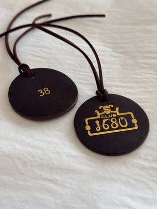 Two black leather tags with gold text and logo on a white fabric background