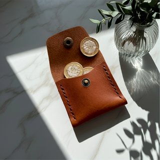 Brown leather coin purse with pound coins on a marble surface with a vase of leaves.