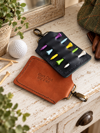 A leather golf teed holder keychain with brass clips, shown open to reveal colorful golf tees inside. The holder has one piece of brown leather and one dark navy piece, both embossed with 'Best Dad Ever'.