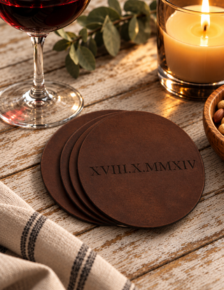 Four round dark brown leather coasters stacked on a rustic wooden table, with the Roman numerals 'XVIII.X.
