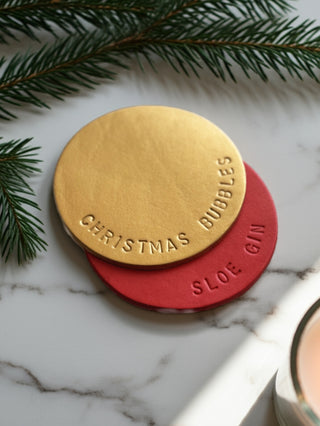 Two round drink markers, one gold and one red, on a marble surface with greenery.