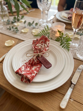 Elegant table setting with a red patterned napkin, white plate, and glass of champagne.