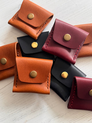 Collection of small leather pouches in various colors with gold buttons on a light wooden surface.