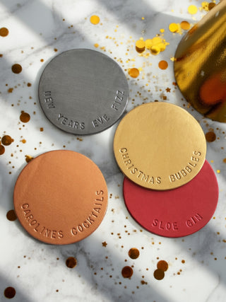 Four round metal coasters with text on a marble surface with gold confetti.