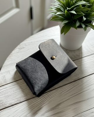 Navy leather card pouch with a gold button on a wooden table next to a potted plant.