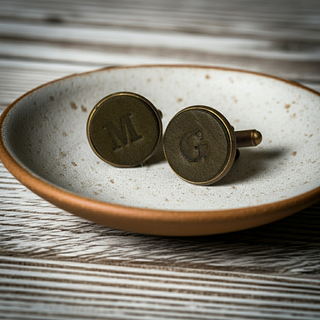 Olive Green Leather Bronze cufflinks with initials 'M' and 'G' on a ceramic dish.