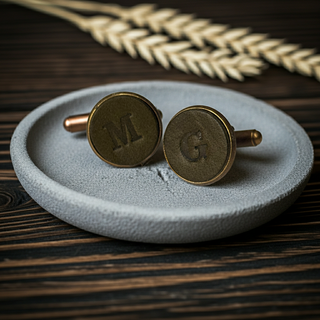 Olive Green Leather cufflinks with initials 'M' and 'G' on a textured gray dish, wooden background