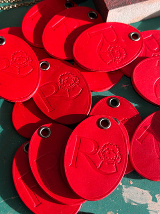 Stack of red keyrings with embossed design on a green surface