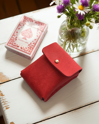 Red leather deck of cards wallet on a white wooden table with playing cards and flowers.