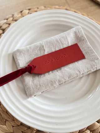 A folded light beige linen pouch with a red leather tag and red ribbon, embossed with the brand name ROSALIND, resting on a white plate.