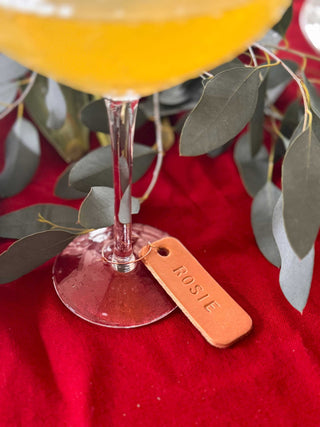 Cocktail in a glass with a 'Rosie' tag on a red surface with eucalyptus leaves.