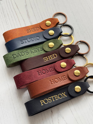 Set of leather keychains with various text engravings on a light wooden surface.