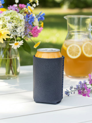 Can in a blue sleeve on a table with flowers and a pitcher in the background