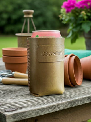 Olive Green leather can holder with 'GRANDPA' engraving on a wooden table outdoors.