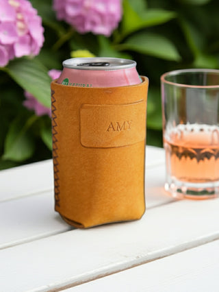 Yellow leather can cooler with 'AMY' branding on a white surface with flowers and a glass in the background.