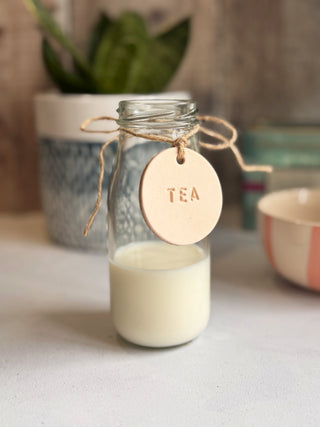 Handmade round leather label with "MILK" embossed, attached to a glass bottle with jute string. Ideal for rustic kitchen styling, pantry storage, or customisable home organisation