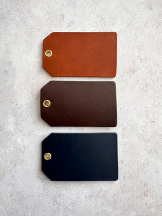 Three leather tags in tan, navy and dark brown on a light gray surface.