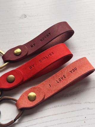 Three leather keychains with hand stamped messages on a leather keyring on a white surface