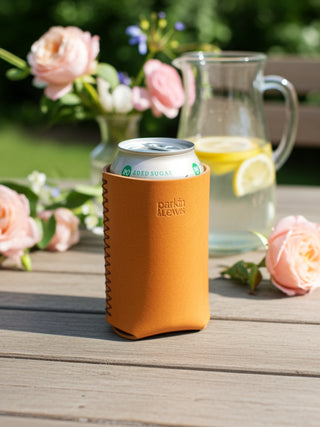 Can in an yellow sleeve on a wooden table with flowers and a pitcher in the background