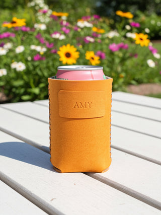 Yellow can cooler with 'AMY' branding on a wooden table with flowers in the background